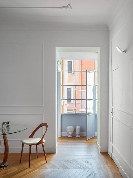 Minimalist interior with glass partition, wood furniture, and herringbone hardwood floors.