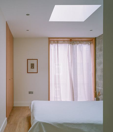 Minimalist bedroom with wooden framing, white curtains, and a skylight above the bed.