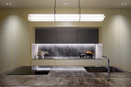 A sleek, modern kitchen with a linear lighting fixture, dark cabinetry, and a marble countertop.