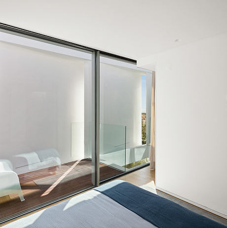 Minimalist bedroom with floor-to-ceiling glass panels, wooden flooring, and neutral decor.