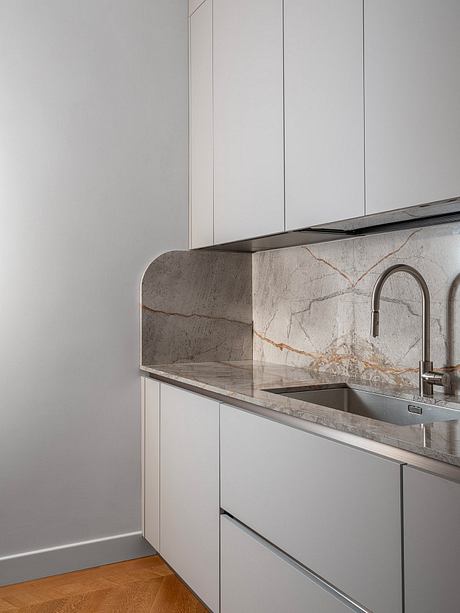 A modern kitchen with sleek white cabinetry, a marble-like backsplash, and a stainless steel sink.
