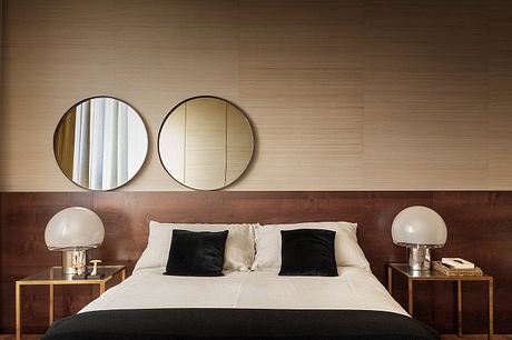 A cozy bedroom with round mirrors, wooden headboard, and contemporary table lamps.