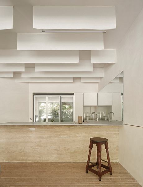 A modern, minimalist kitchen with clean lines, floating shelves, and a wooden stool.