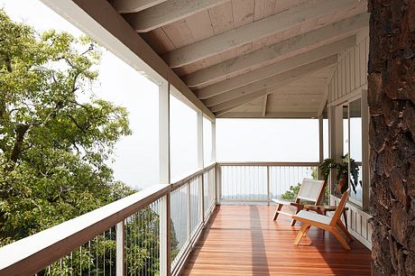 Wooden porch with railing overlooking lush greenery, showcasing rustic architecture.