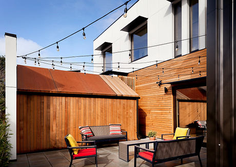 Sleek modern outdoor patio with wood siding, string lights, and minimalist furniture.