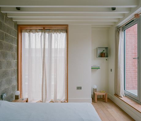 Minimalist bedroom interior with wooden beams, curtains, and contemporary furnishings.