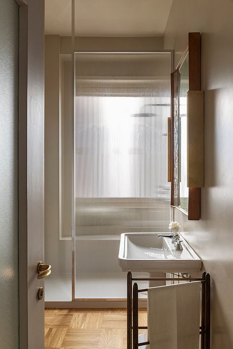 A modern, minimalist bathroom with a frosted glass partition, wooden accents, and a pedestal sink.
