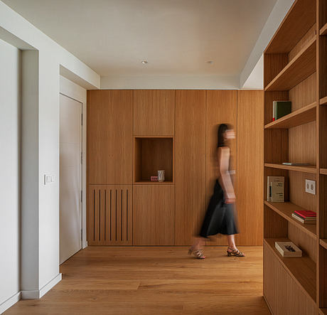 Minimalist interior design with warm wood paneling, built-in shelving, and a blurred figure moving.