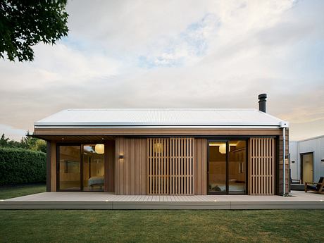 A modern, minimalist wooden cabin with a slatted facade, surrounded by lush greenery.