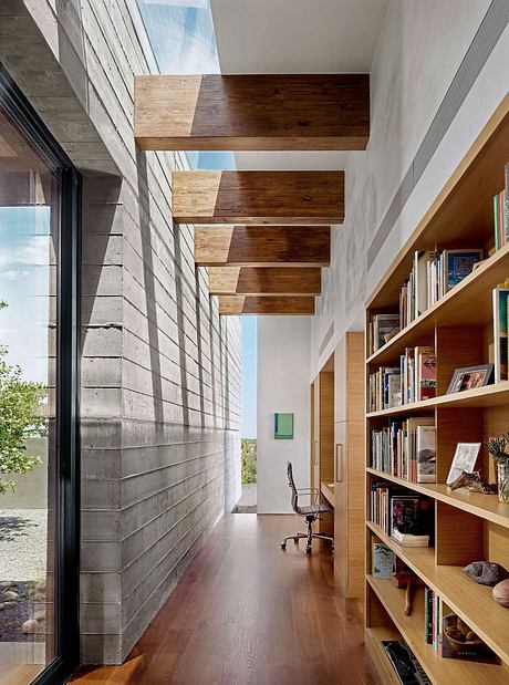 Concrete walls, wooden beams, and a bookshelf-lined hallway with a view of the outdoors.