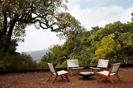 Serene outdoor seating area with wooden chairs and fire pit surrounded by lush vegetation.