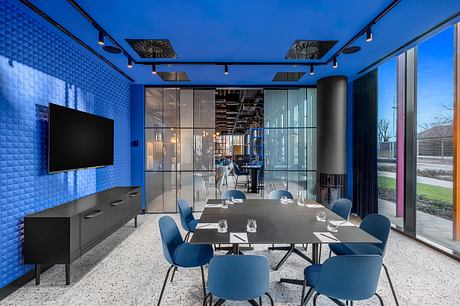 Modern conference room with geometric blue walls, sleek furniture, and large windows overlooking greenery.