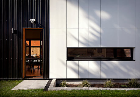 Sleek, modern facade with wooden accents and recessed windows; minimalistic landscaping.