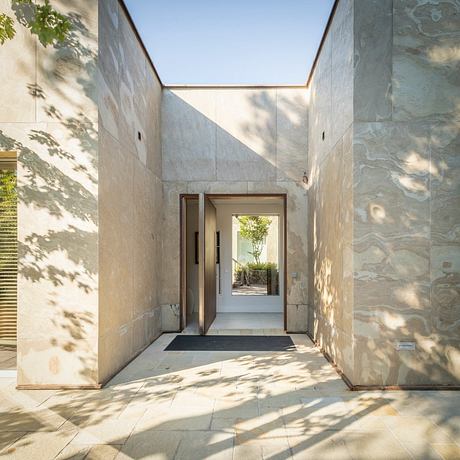 An entryway with a minimalist design, featuring natural stone walls, recessed lighting, and a framed garden view.