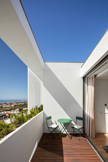 Minimalist balcony with wooden floor, green chairs, and panoramic city view through glass walls.