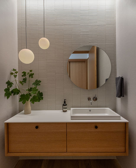 Sleek, modern bathroom design with wooden vanity, circular mirror, and pendant lights.