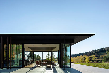 Modern glass-walled pavilion with sleek, angular design overlooking scenic countryside.