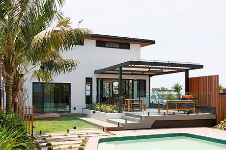 Contemporary tropical home with sleek glass walls, elevated patio, and in-ground pool.