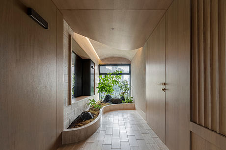 A modern, minimalist hallway with a curved window, plants, and tile flooring.