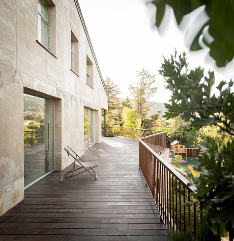 A modern stone building with a wooden deck overlooking a lush, forested landscape.