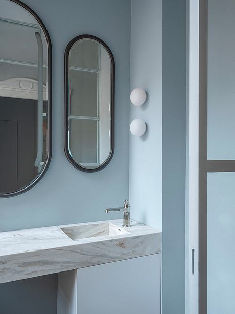 Minimalist bathroom design with oval mirrors, marble vanity, and modern lighting.