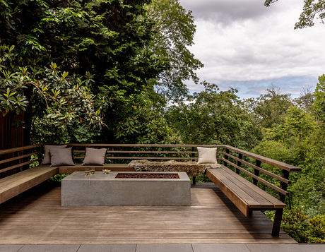 Cozy outdoor seating area with wooden benches, concrete fire pit, and lush foliage backdrop.