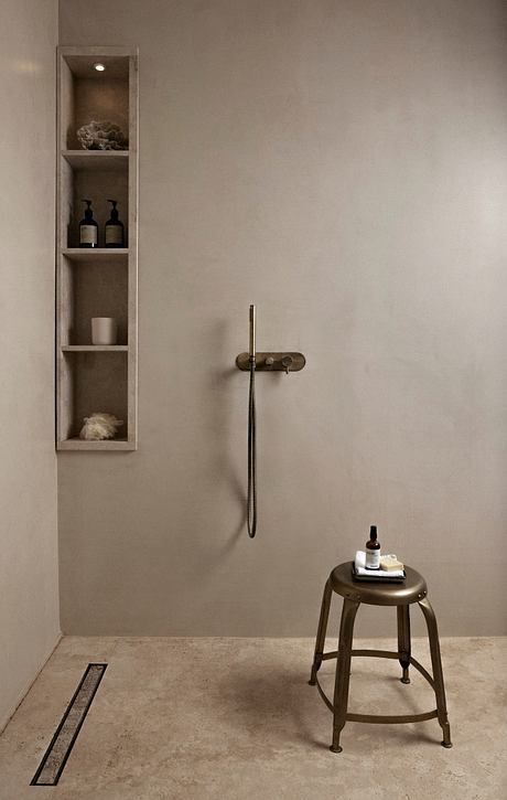 Minimalist bathroom design with recessed shelving, wall-mounted fixtures, and industrial stool.