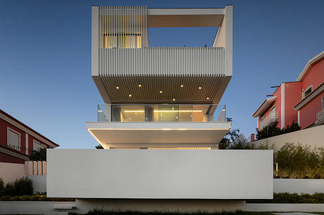 Modern, sleek building with elevated, illuminated outdoor terrace and glass facade.