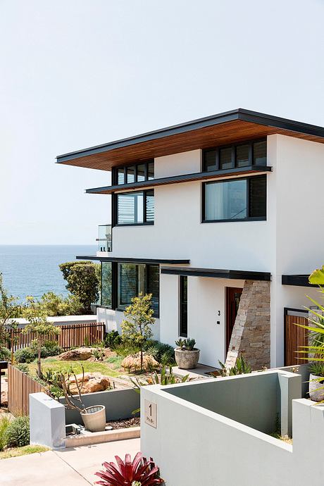 Contemporary coastal home with sleek wood-accented exterior, expansive windows, and lush landscaping.