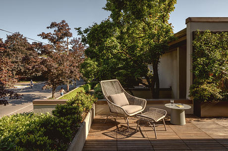 Cozy outdoor seating area with rattan furniture, surrounded by lush greenery and a paved patio.