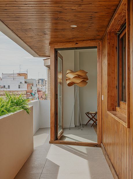 Modern wooden interior with a sculptural light fixture, potted plant, and concrete floor.