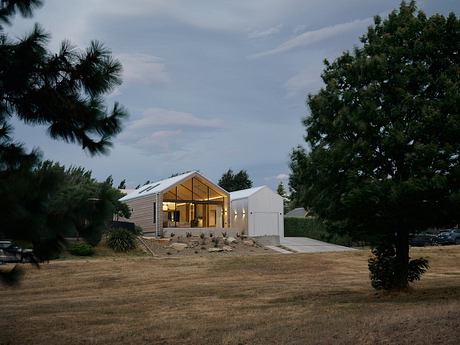 A contemporary rural home with gabled roofs, large windows, and a wraparound porch.