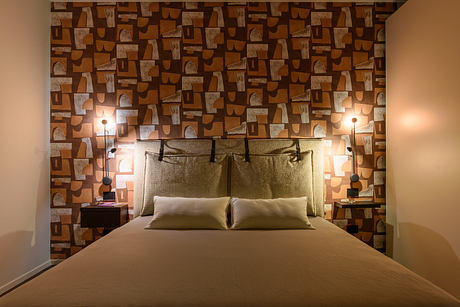 Warm, inviting bedroom with textured stone wall, bedframe, and task lighting.