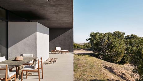 Minimalist concrete structure with large windows overlooking a grassy landscape.
