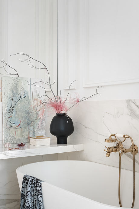 Elegant marble bathroom with modern black vase, gold fixtures, and patterned towel.