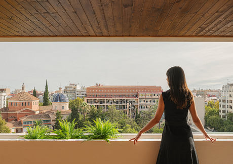Panoramic cityscape view from a balcony, featuring domed roofs, greenery, and modern buildings.