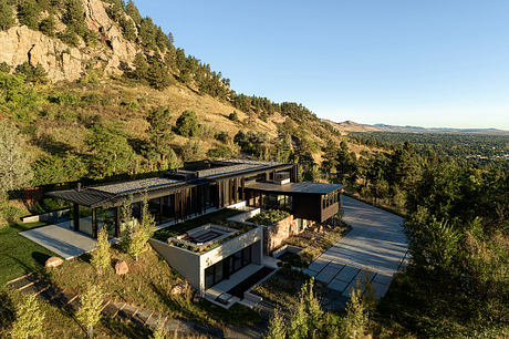 A modern, hillside residence with expansive windows, terraces, and a natural, wooded setting.