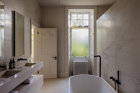 Spacious bathroom with marble walls, vessel sink, and large window allowing natural light.