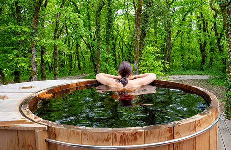 A rustic wooden hot tub nestled in a lush green forest, creating a serene outdoor oasis.