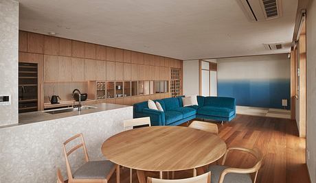 A modern, open-concept living space with sleek wood paneling, a blue sectional, and a round dining table.
