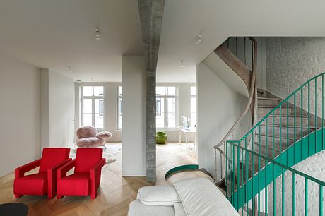 Bright, airy loft-style interior with exposed concrete beams, vibrant red chairs, and a turquoise staircase.