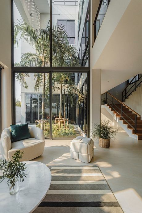 Spacious modern living room with tall glass walls, lush palm trees, and minimalist furniture.