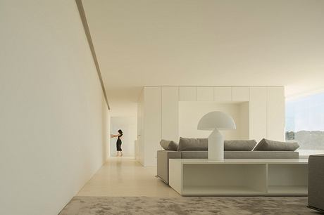 Modern, minimalist living room with clean lines, built-in furniture, and a glimpse of a person in the distance.