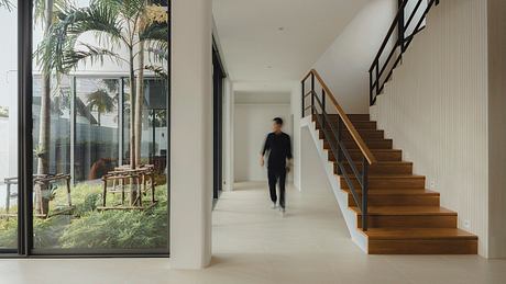 A modern, open-concept home with wooden stairs, glass walls, and lush indoor greenery.
