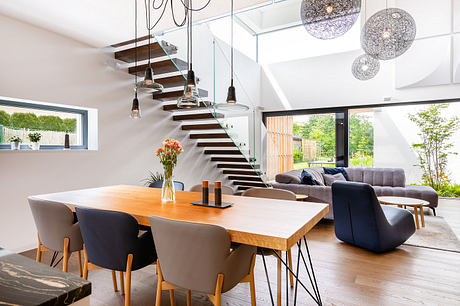 Spacious modern living area with open-plan design, wood-and-glass staircase, and statement lighting.