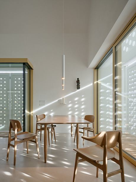 A modern, minimalist dining area with wooden furniture and natural lighting from floor-to-ceiling windows.