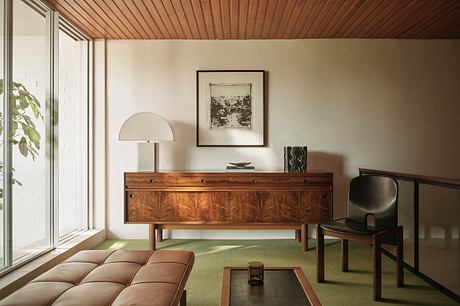 A cozy, mid-century inspired room with a wooden ceiling, an ornate sideboard, and a modern lamp.