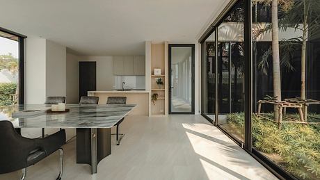 Modern open-plan kitchen with dining area, large windows overlooking lush greenery.