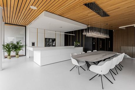 Sleek modern kitchen with monochrome palette, geometric lighting, and wood-paneled ceiling.
