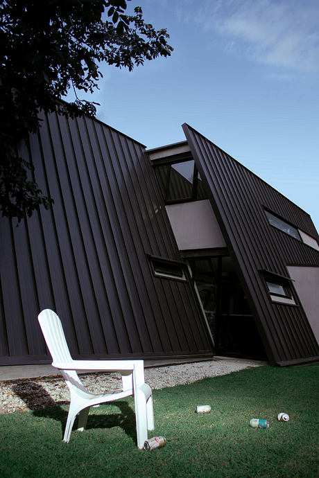 A modern, angular building with a striking dark facade and contrasting white chair.